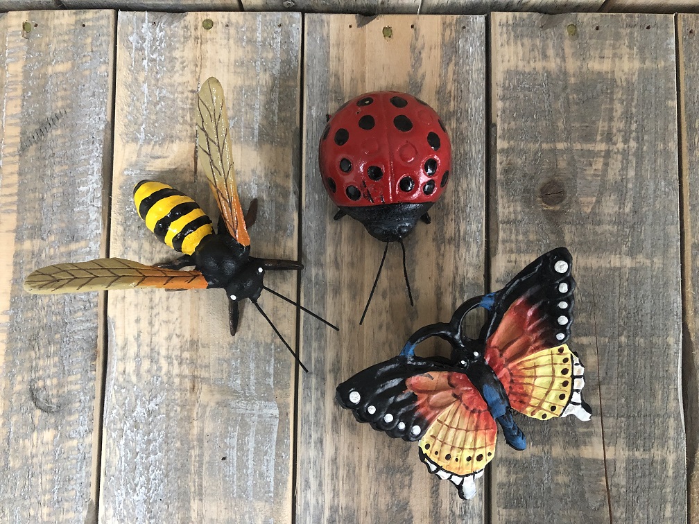 Gietijzeren beeldjes van een bij, vlinder en een lieveheersbeestje, vol in kleur.