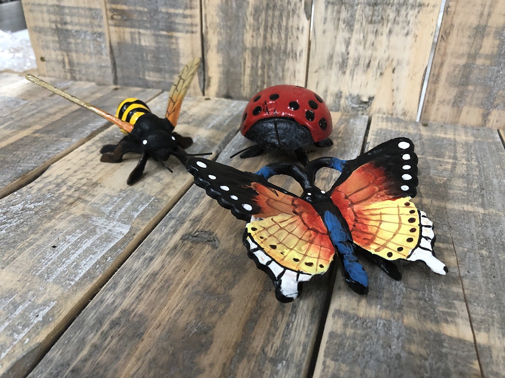 Gietijzeren beeldjes van een bij, vlinder en een lieveheersbeestje, vol in kleur.