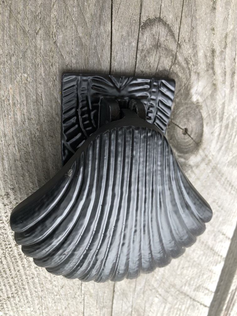 Decoratieve deurklopper in de vorm van een schelp, geheel metaal zwart. 